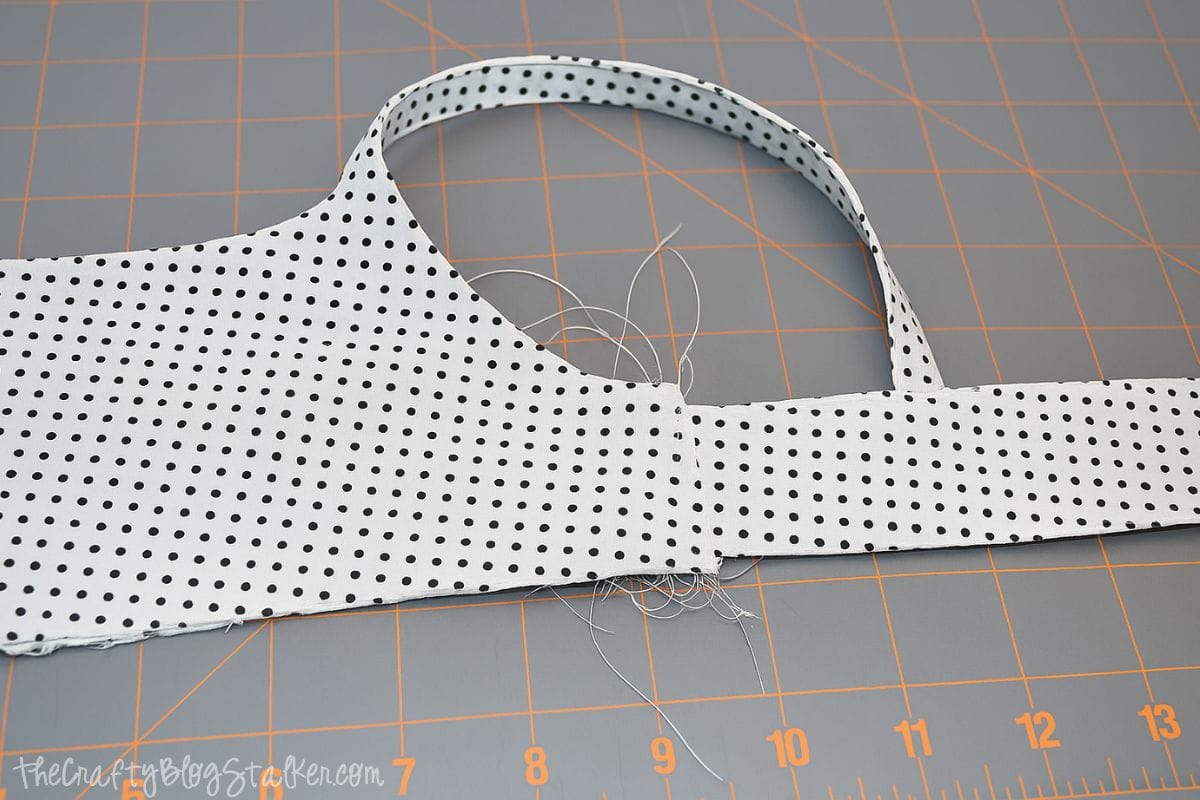 Sewn polka-dot tank top bodice with one strap attached, showing white thread and gathered stitching on a gridded cutting mat for sewing.