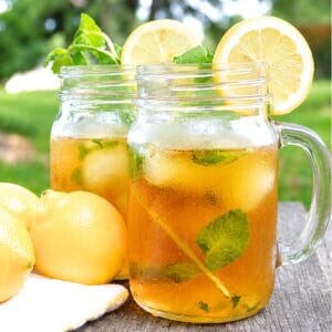 Two mason jars of iced tea with lemon slices, mint leaves, and ice on a picnic table.