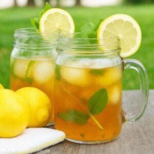 Two mason jars of iced tea with lemon slices, mint leaves, and ice on a picnic table.