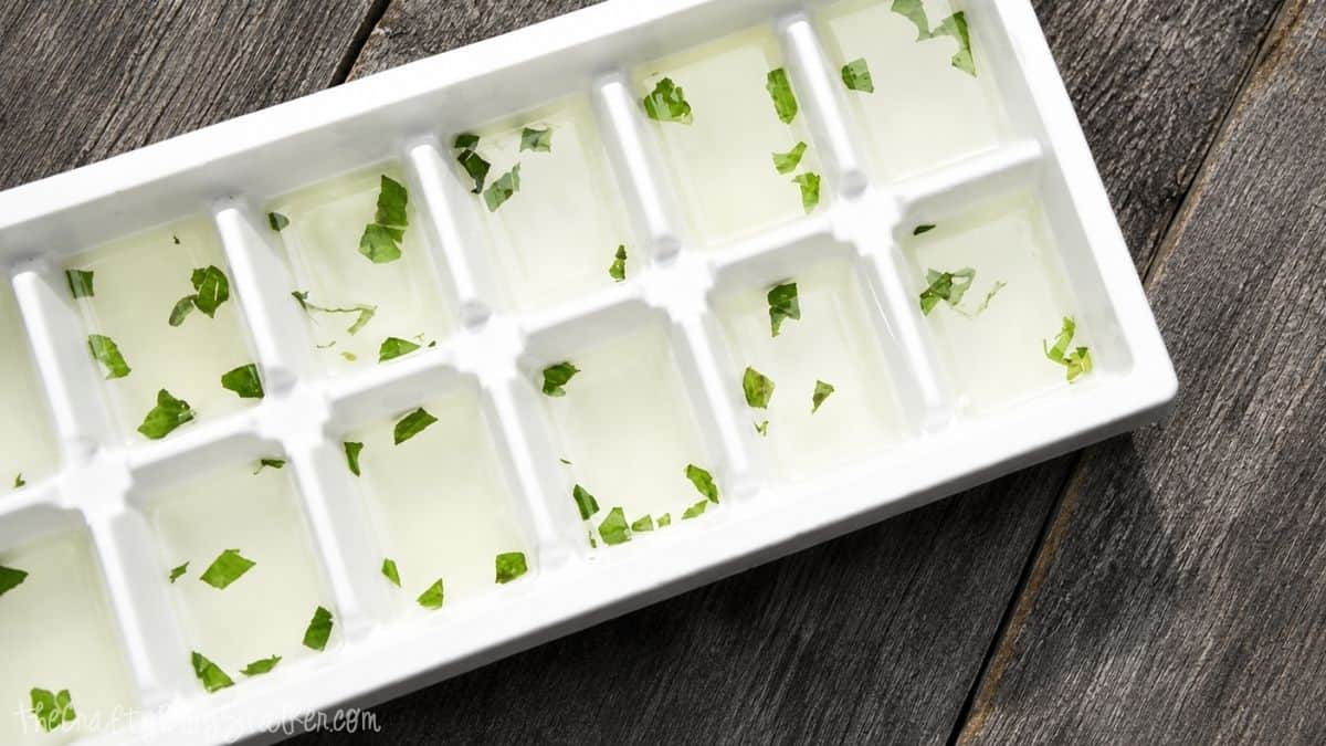 White ice cube tray filled with lemonade and chopped mint leaves in each compartment, ready to be frozen on a wooden surface.