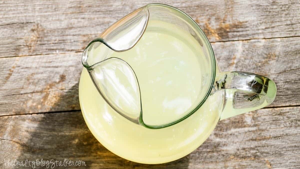 An easy Iced Tea Recipe with Lemonade Ice Cubes & Mint Leaves! Absolutely delicious! #AmericasTea #shop A clear glass pitcher filled with homemade lemonade, shown from above on a rustic wooden surface.