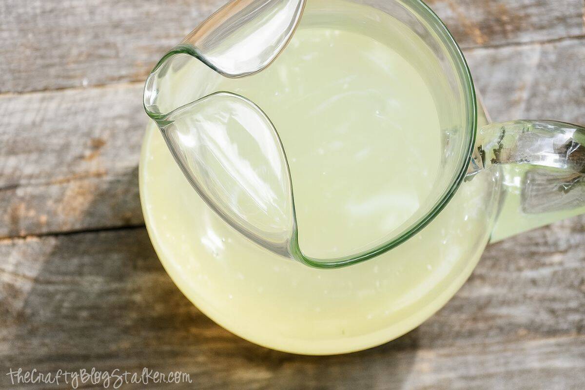 A clear glass pitcher filled with homemade lemonade, shown from above on a rustic wooden surface.
