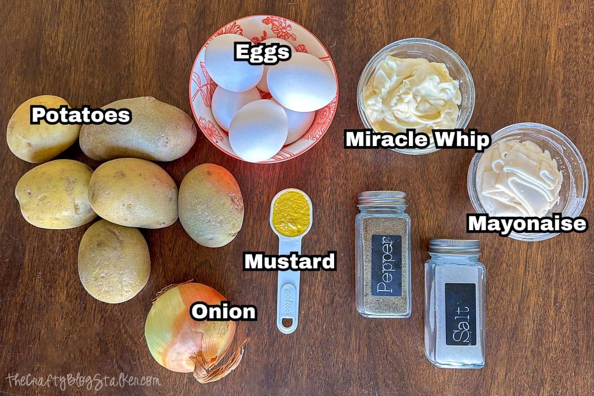 Top-down view of labeled potato salad ingredients on a wooden table: potatoes, eggs, onion, mustard, Miracle Whip, mayonnaise, salt, and pepper.
