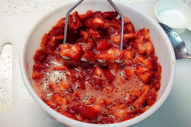 mashing strawberries with a potato masher