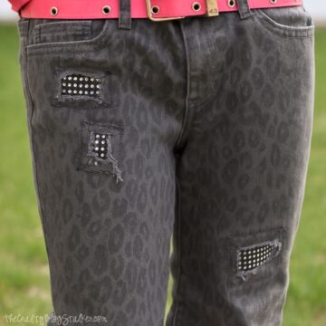 Gray leopard-print jeans with three distressed patches backed by sparkly rhinestone fabric, paired with a bright pink belt.