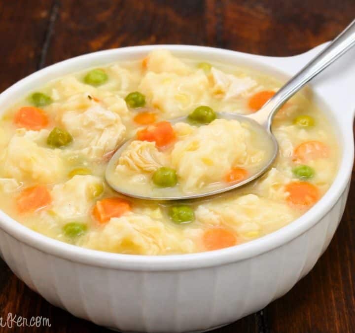 Homemade chicken and dumplings in a white bowl with tender chicken, fluffy dumplings, peas, and carrots in a creamy broth on a wooden table