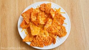 Plate of tortilla chips topped with melted cheese on a wooden table.
