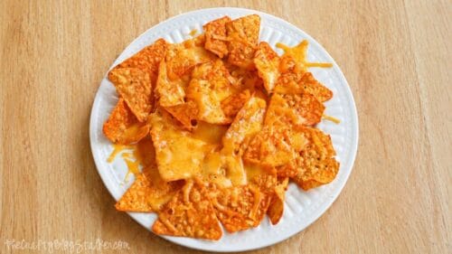 Plate of tortilla chips topped with melted cheese on a wooden table.
