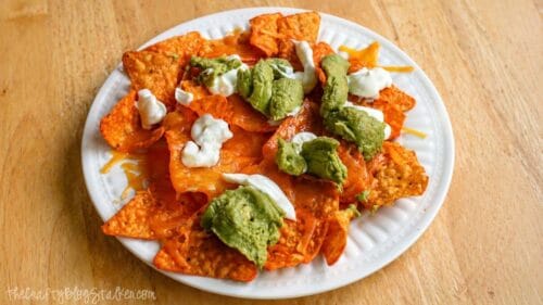 Plate of nachos topped with melted cheese, guacamole, and sour cream on a wooden table.