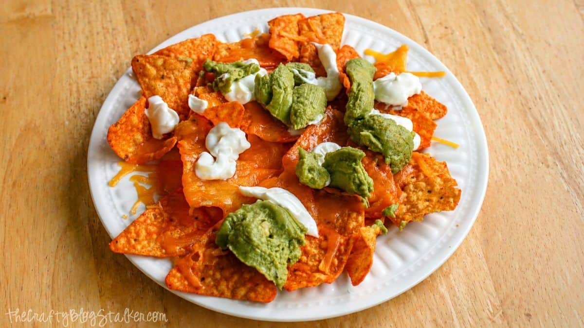 Plate of nachos topped with melted cheese, guacamole, and sour cream on a wooden table.