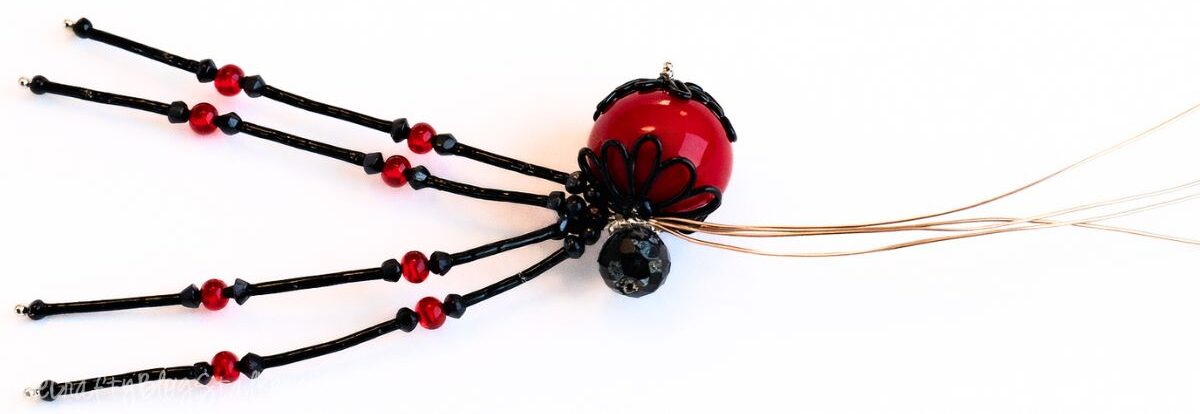 Half assembled beaded spider craft with wire legs, bead body, and loose wire ends extending from the center during assembly.