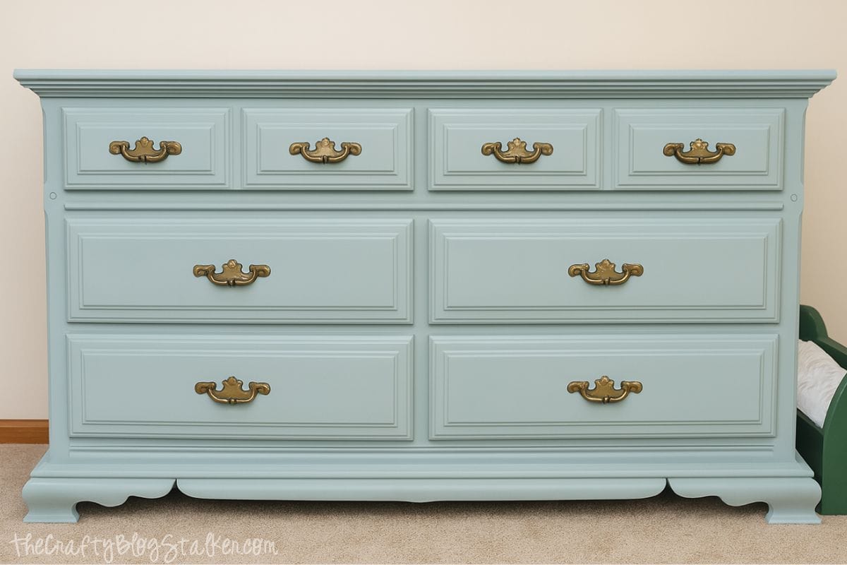 A refinished light blue dresser with vintage-style brass handles, sitting on a carpeted floor against a cream-colored wall.