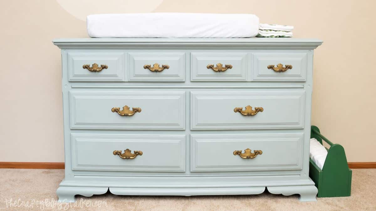 A refinished light blue dresser with vintage-style brass handles, sitting on a carpeted floor against a cream-colored wall.