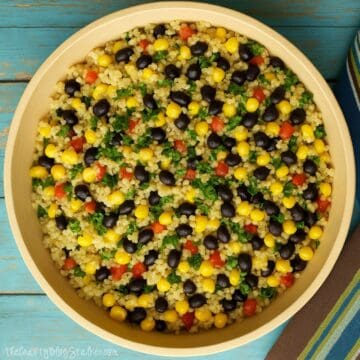 Overhead view of a bowl filled with colorful quinoa salad made with black beans, corn, red pepper, and chopped herbs on a turquoise wooden background.