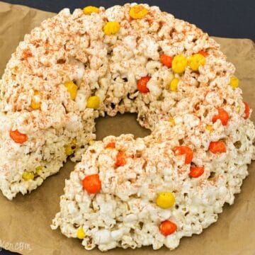 A round popcorn cake made with candy corn and coated in marshmallow, resting on brown parchment paper.