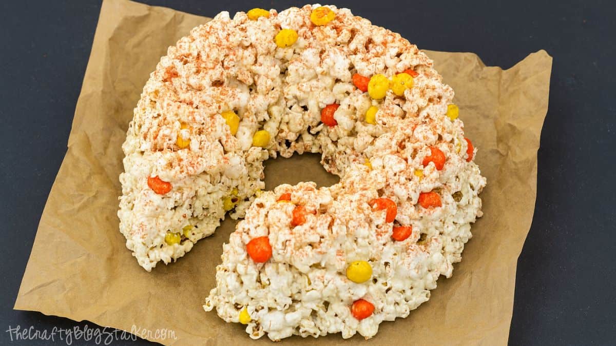 Halloween Popcorn cake made with White Chocolate Candy Corn M&M's  A round popcorn cake made with candy corn and coated in marshmallow, resting on brown parchment paper.