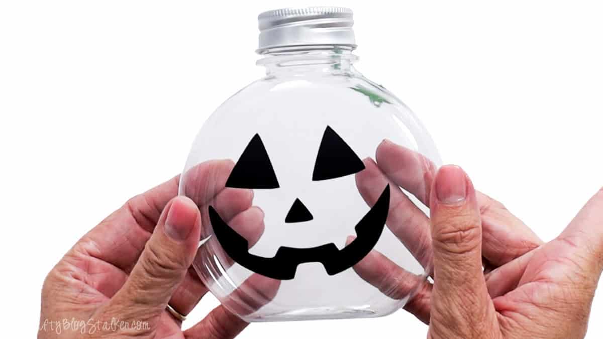 Clear pumpkin-shaped jar decorated with a black vinyl jack-o'-lantern face, ready to be filled with Halloween candy.