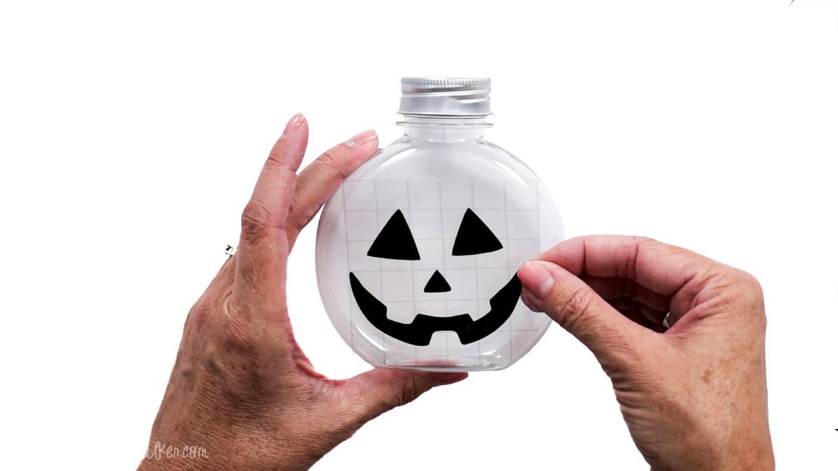 Applying a black vinyl jack-o'-lantern face to a clear pumpkin-shaped candy jar using transfer tape.