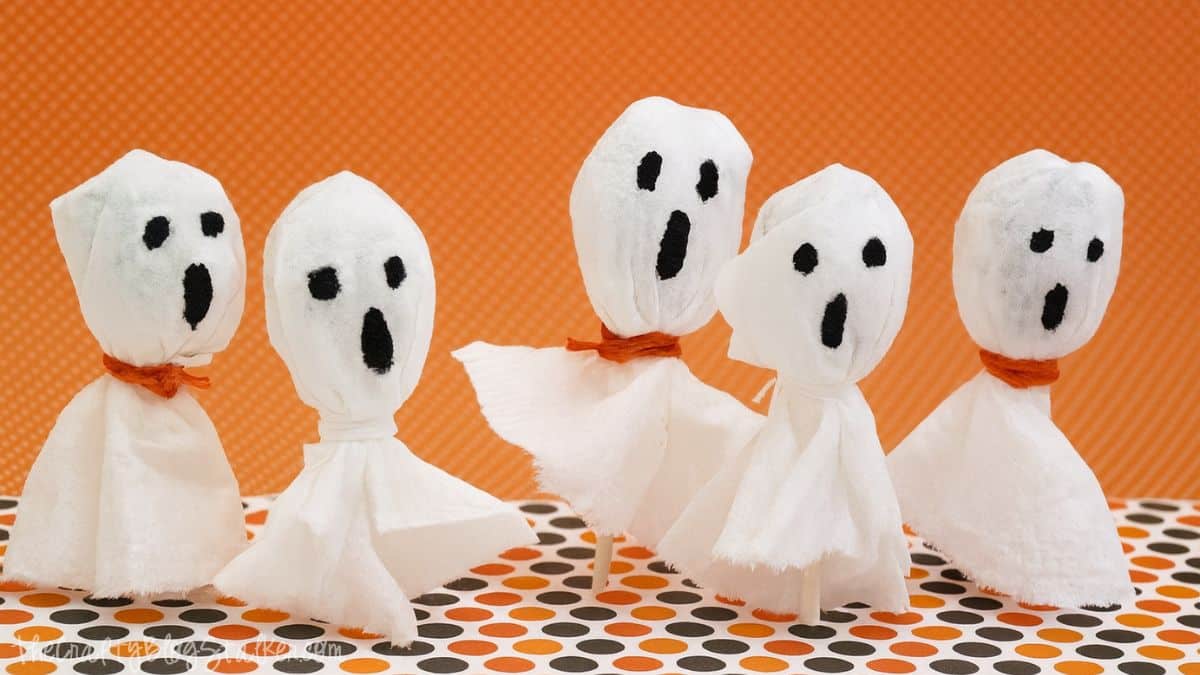Celebrate Halloween with these cute Spooky Ghost Suckers. A GREAT last minute treat idea! Five lollipop ghost crafts made from tissues and tied with string, displayed on a polka dot surface with an orange background.