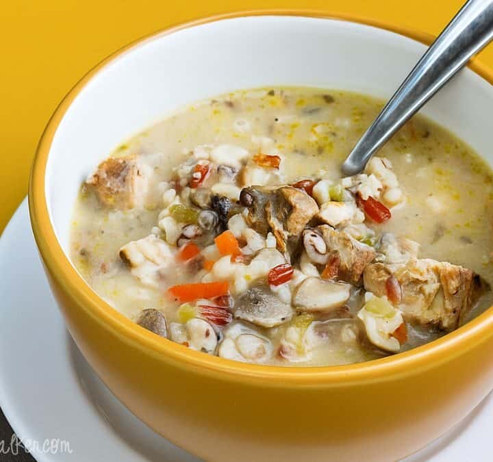 Bowl of creamy grilled chicken and wild rice soup with vegetables and a spoon, served in a yellow bowl on a white plate.