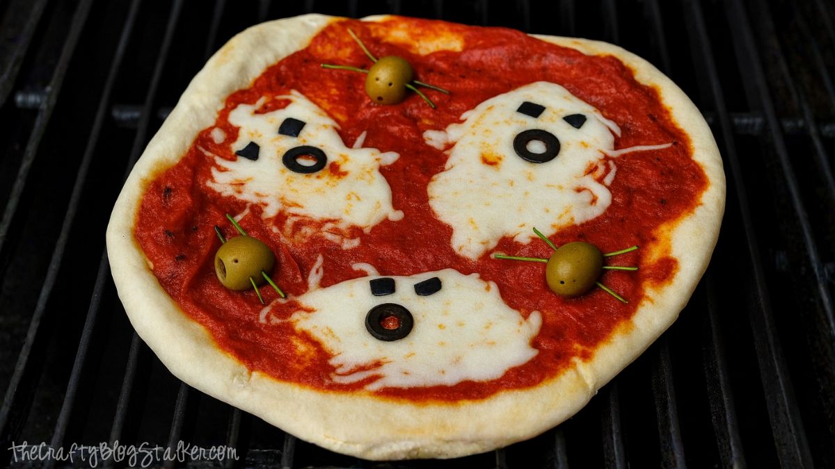 Grilled Halloween pizza with cheese ghosts and olive spiders. Too cute! This kids will love this! : ) Halloween pizza topped with ghost-shaped melted cheese, black olive eyes and mouths, and green olive spiders on tomato sauce.