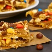 Close-up of Halloween candy saltine toffee topped with M&M's, peanuts, and caramel toffee layers, cut into squares and served on parchment paper.