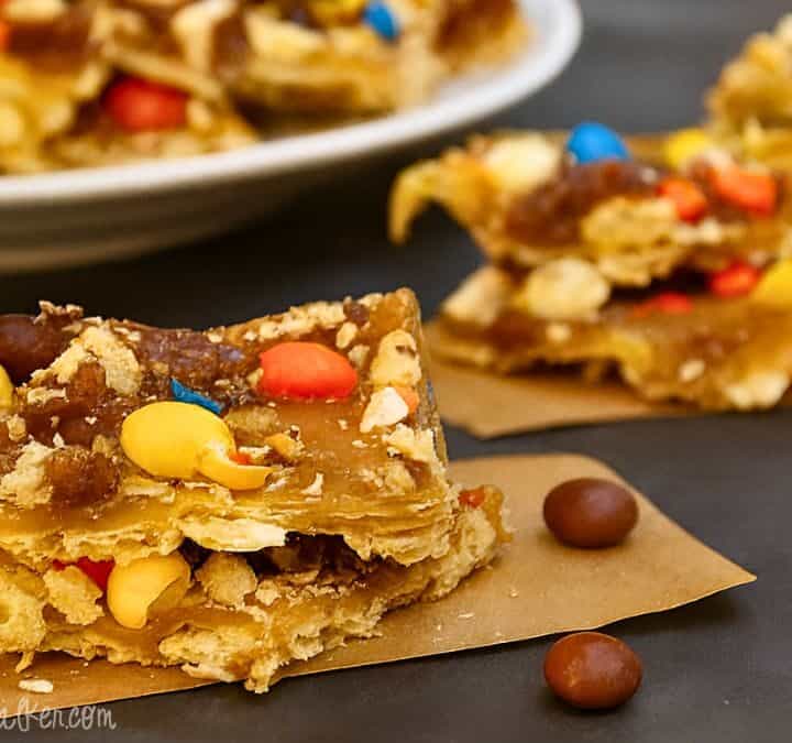 Close-up of Halloween candy saltine toffee topped with M&M's, peanuts, and caramel toffee layers, cut into squares and served on parchment paper.