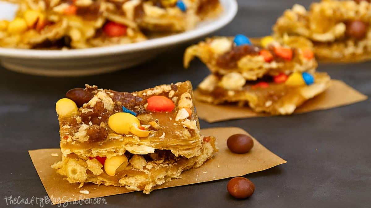 Pieces of Halloween candy toffee made with crackers, caramel, and colorful candies, stacked on parchment paper.