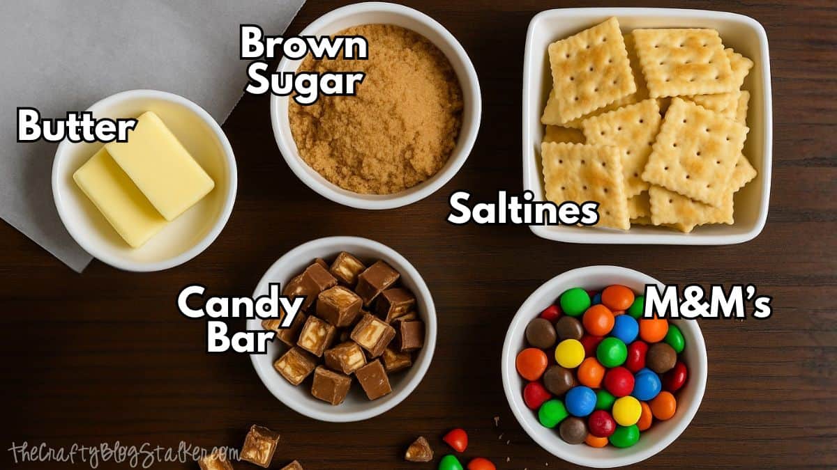 Overhead view of ingredients for saltine toffee including butter, brown sugar, saltine crackers, chopped candy bars, and colorful M&M's in small bowls on a wooden table.