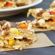 Pieces of Halloween candy toffee made with crackers, caramel, and colorful candies, stacked on parchment paper.