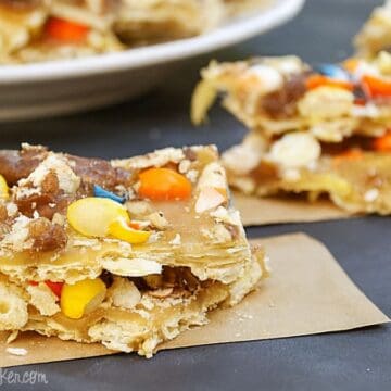 Pieces of Halloween candy toffee made with crackers, caramel, and colorful candies, stacked on parchment paper.