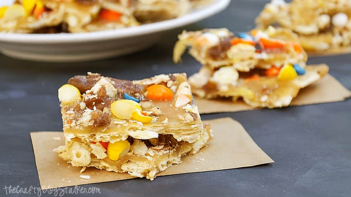 Halloween Toffee Recipe for your Halloween celebrations via cherishedbliss.com #SpookyCelebration #shop Pieces of Halloween candy toffee made with crackers, caramel, and colorful candies, stacked on parchment paper.