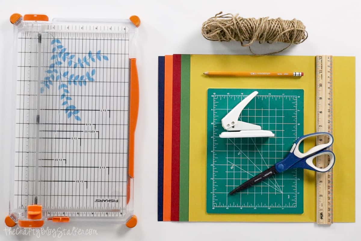 Supplies used to make a paper banner; cardstock, paper trimmer, scissors, twine, and a hole punch.