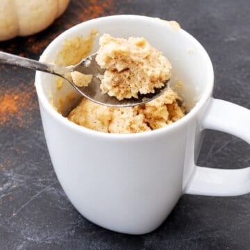 Close-up of pumpkin spice mug cake in a white mug with a spoonful of the soft, spiced cake lifted above.