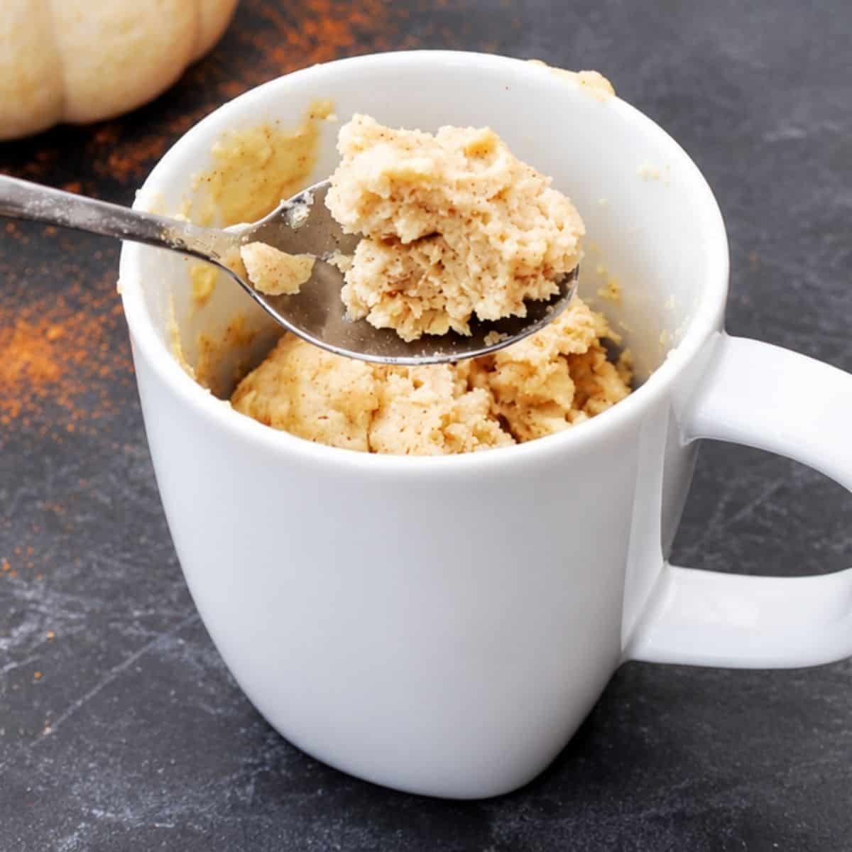 Close-up of pumpkin spice mug cake in a white mug with a spoonful of the soft, spiced cake lifted above.