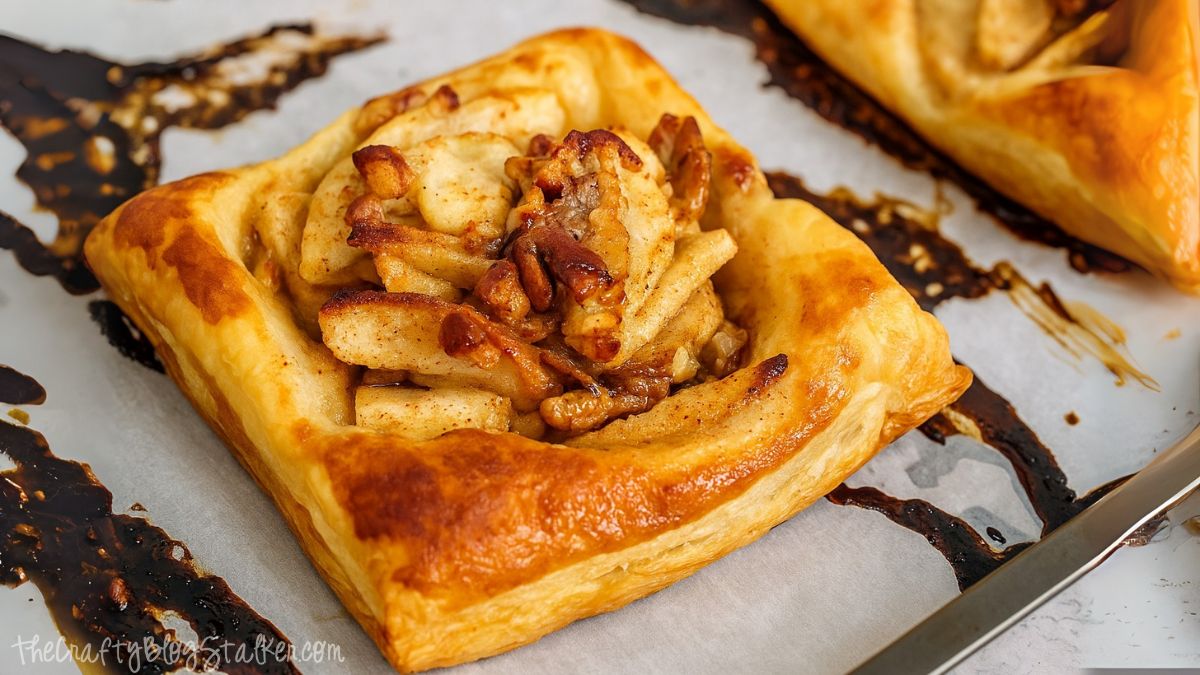 Golden brown puff pastry filled with sliced apples, pecans, and cinnamon on a parchment-lined baking sheet.