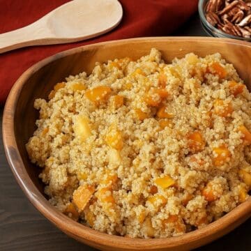 Wooden bowl filled with butternut squash quinoa salad, showing cooked quinoa mixed with soft orange squash pieces on a dark tabletop.