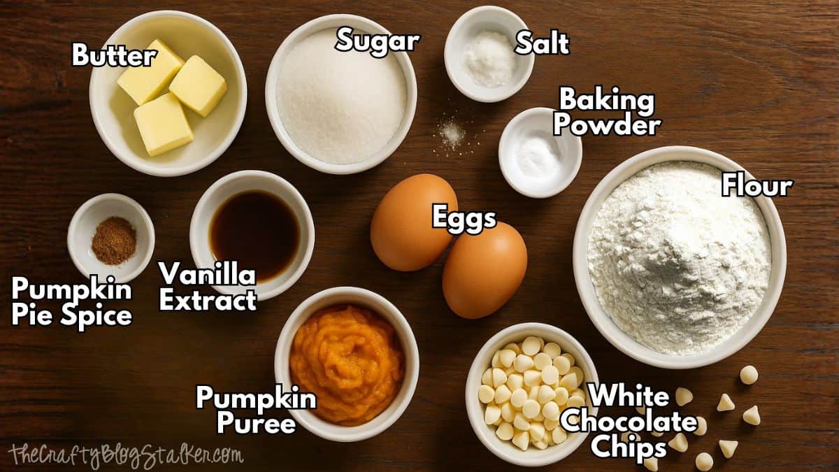 Labeled ingredients for pumpkin biscotti arranged on a wooden surface, including flour, sugar, butter, eggs, pumpkin puree, spices, vanilla, and white chocolate chips.