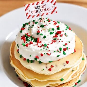 Stack of Christmas chocolate chip pancakes topped with whipped cream, red and green holiday sprinkles, and a Merry Christmas flag pick.