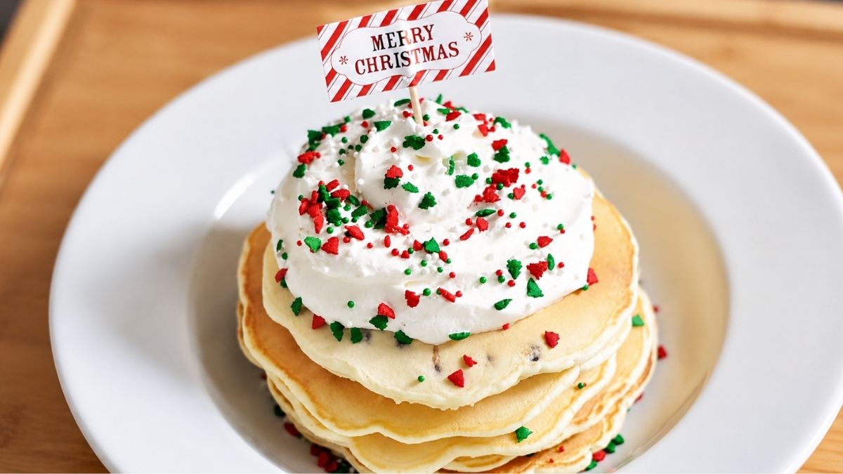 Stack of Christmas chocolate chip pancakes topped with whipped cream, red and green holiday sprinkles, and a Merry Christmas flag pick.