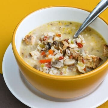 Bowl of creamy grilled chicken and wild rice soup with mushrooms, carrots, and vegetables, served with a spoon in a yellow bowl.