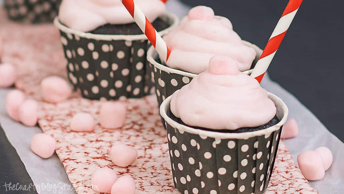 Chocolate cupcakes topped with fluffy pink peppermint marshmallow frosting, served in black polka dot cups with red and white striped straws.