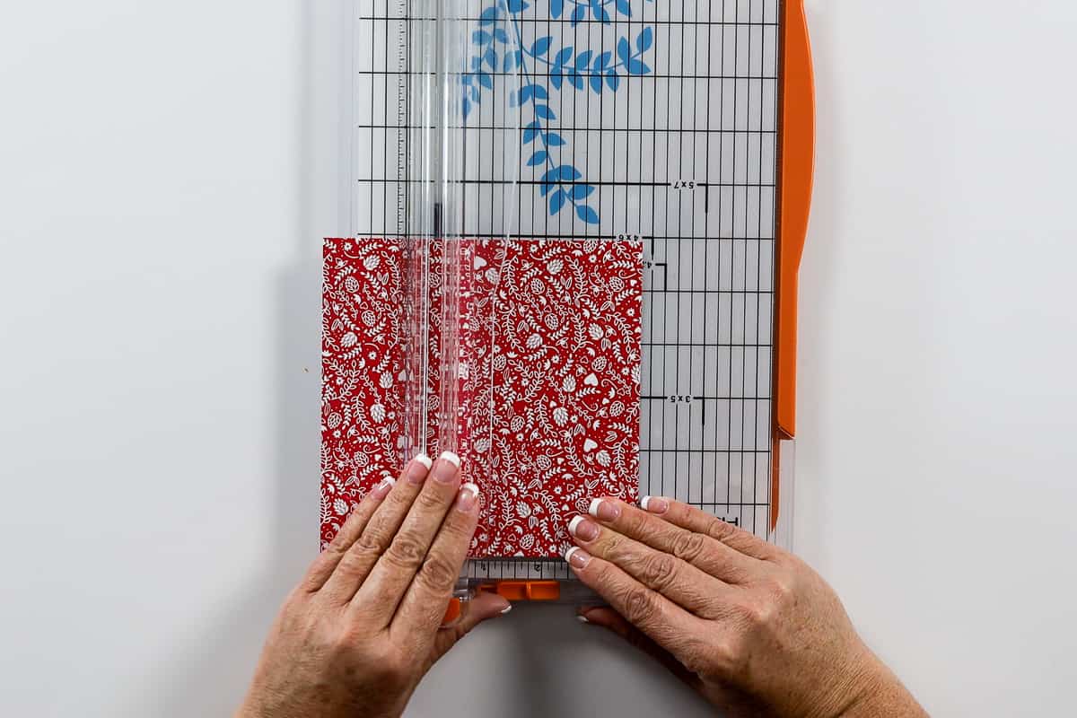 Cutting a piece of red patterned paper with a paper trimmer.