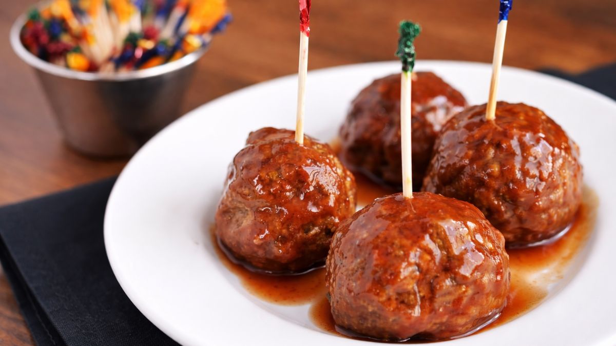 Sweet chili meatball appetizers served on a white plate with toothpicks, coated in glossy sauce, with a small cup of extra picks in the background.