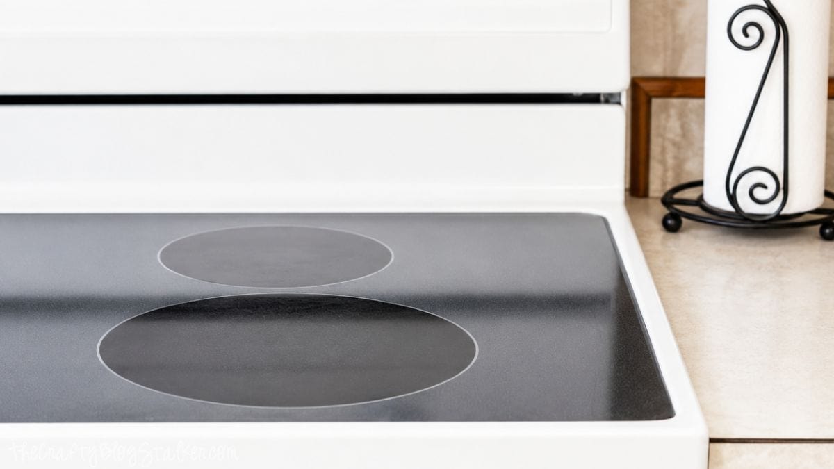 Clean and shiny glass top stove after cleaning with smooth black burners and a spotless surface on a white electric range.
