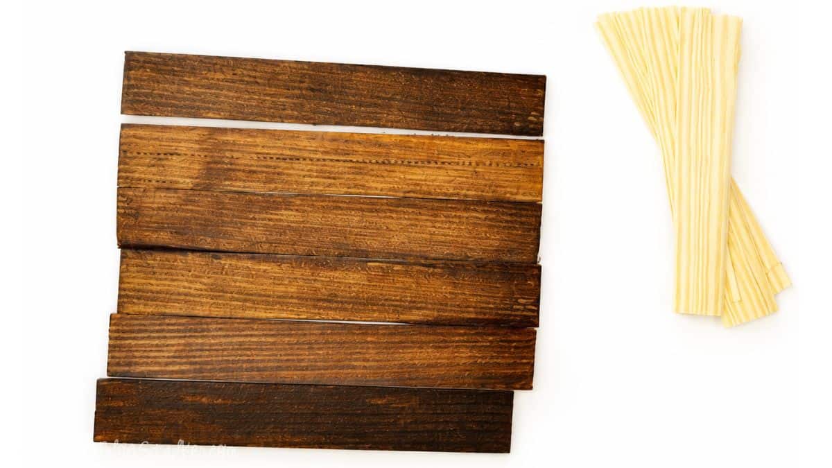 Make new wood look OLD with this tutorial on how to Weather Wood. Click through for instructions Stained wooden planks arranged side by side on a white background, with a small bundle of unfinished wood strips placed to the right.