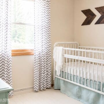 Travel-themed nursery with a white crib, globe on a mint dresser, gray chevron curtains, wood arrow wall decor, and light blue bedding.