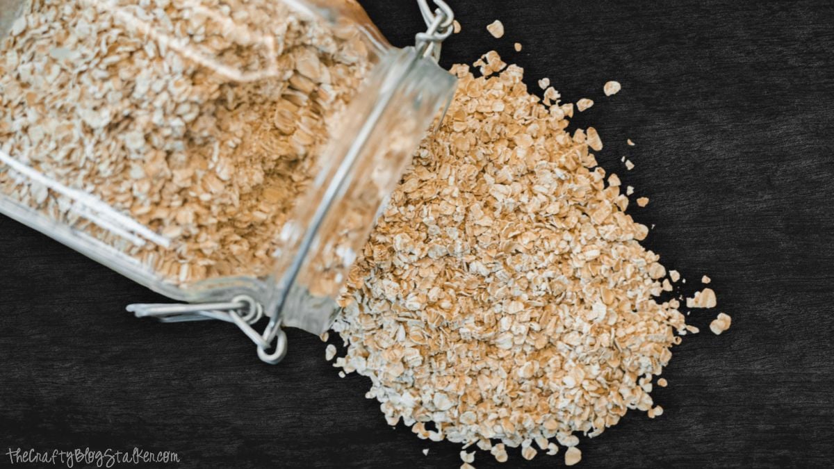 A glass jar tipped on its side with rolled oats spilling onto a dark wooden tabletop.