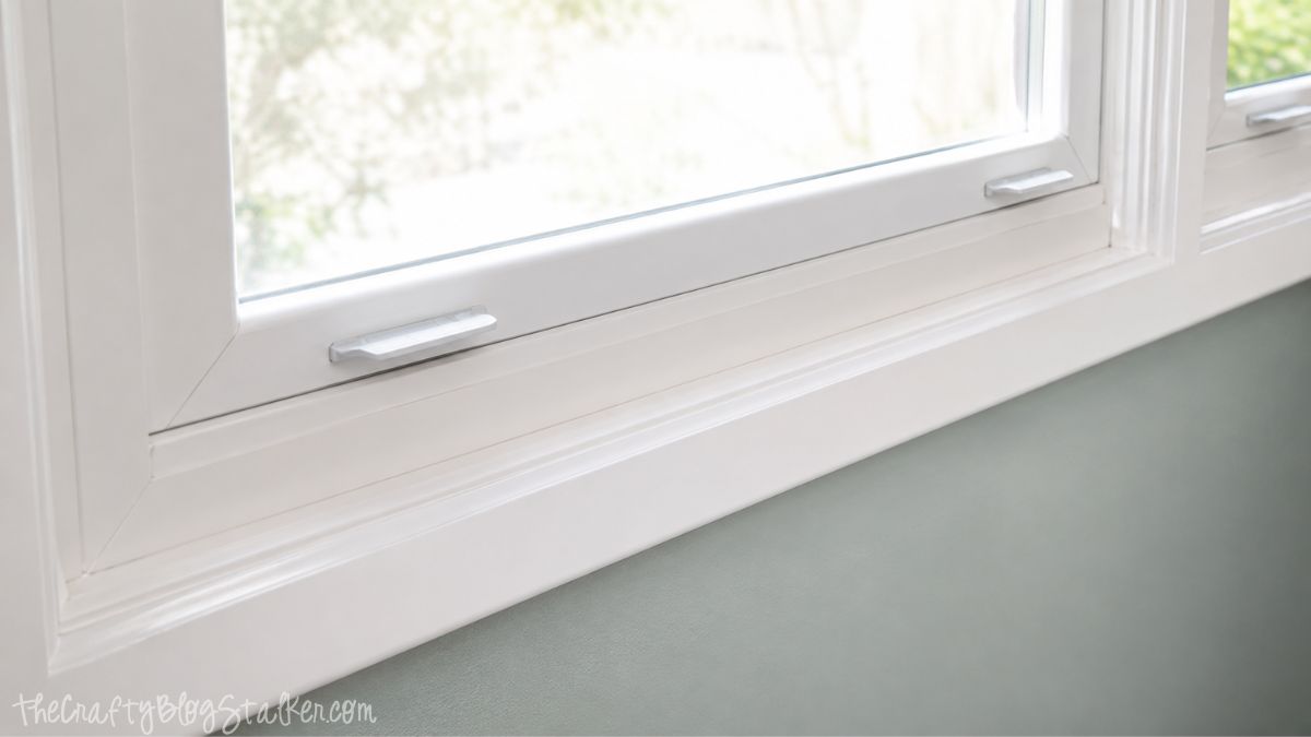 Close-up of a white painted window trim and sill above a light green wall, showing clean molding details and a freshly finished surface.