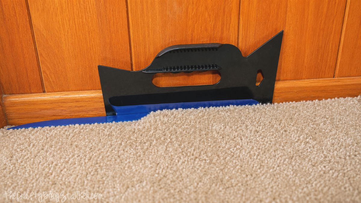 Paint shield tool tucked between carpet and wood baseboard to protect flooring while painting wood trim and paneling.